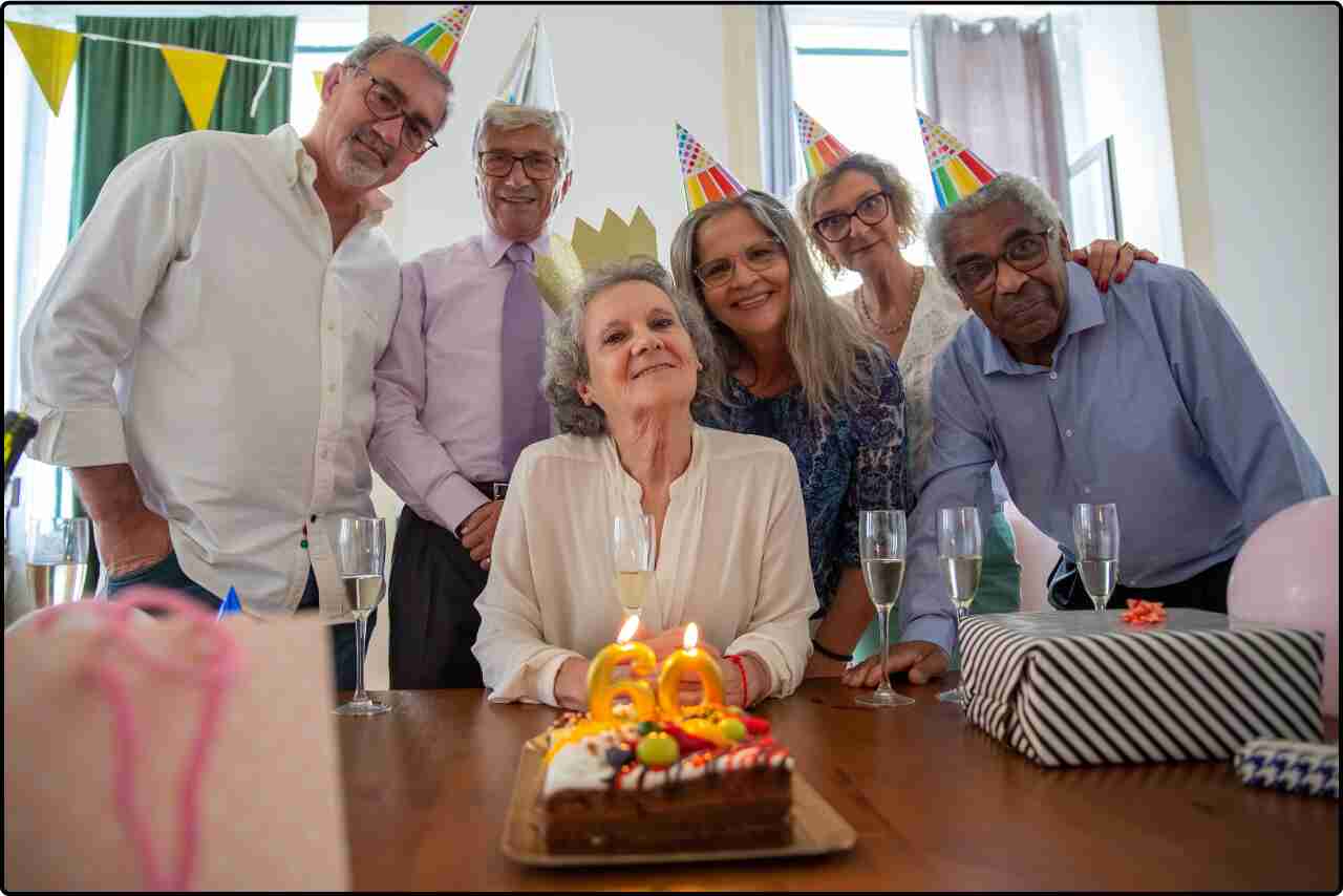 Group of people gathered around an elderly man and woman celebrating a birthday party